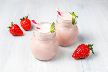 Pink strawberry milkshake in glass jar on wooden background, healthy food for breakfast and snack, strawberry smoothie and scattered strawberry isolated on white, strawberries milkshake, milk shake.