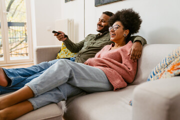 Cheerful couple watching tv together while sitting on couch