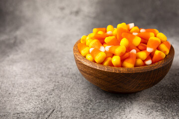 Candy corn. Classic white, orange and yellow Halloween lollipops. Sweet pumpkin gummies in a wooden bowl on a black marble background.Copy space.Place for text. Holiday concept.
