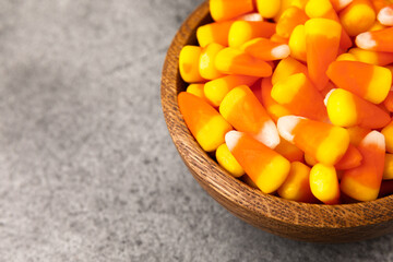 Candy corn. Classic white, orange and yellow Halloween lollipops. Sweet pumpkin gummies in a wooden bowl on a black marble background.Copy space.Place for text. Holiday concept.