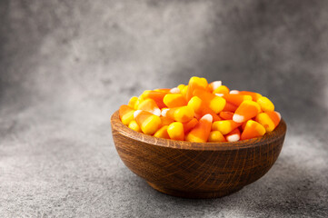 Candy corn. Classic white, orange and yellow Halloween lollipops. Sweet pumpkin gummies in a wooden bowl on a black marble background.Copy space.Place for text. Holiday concept.
