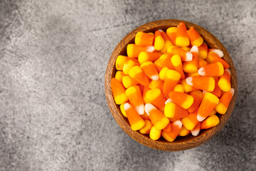 Candy corn. Classic white, orange and yellow Halloween lollipops. Sweet pumpkin gummies in a wooden bowl on a black marble background.Copy space.Place for text. Holiday concept.