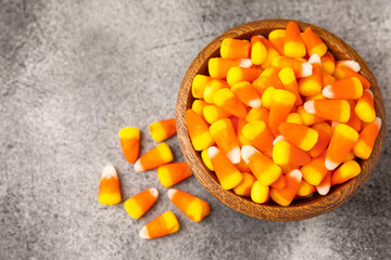 Candy corn. Classic white, orange and yellow Halloween lollipops. Sweet pumpkin gummies in a wooden bowl on a black marble background.Copy space.Place for text. Holiday concept.