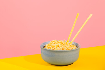 Curly noodles in blue bowl on bright yellow and pink background.