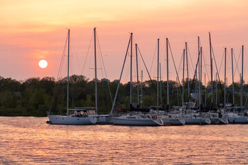 Sunset at Lake Ontario, row of yachts at the marina with bright orange sky, clouds and sun in the background and reflection in foreground. Toronto, Ontario, Canada.