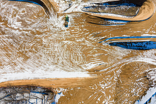 Aerial view of heavy machinery grading a commercial construction site with tire tracks in soil - Powered by Adobe