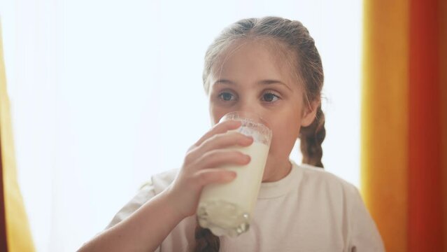 child girl drinks milk from a glass in the kitchen. happy family healthy eating concept. baby girl and glass of milk close-up. child girl enjoying warm milk lifestyle in the kitchen