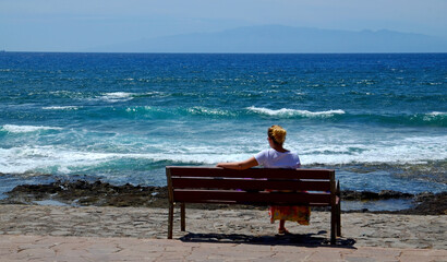 Woman sitting alone on the wooden bench in front of the ocean.Summer vacation, travel concept.