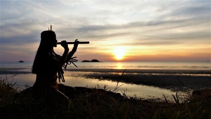 A Native American Indian plays a bamboo flute. Silhouette against the background of sunset. © Alexander