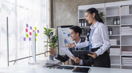 Two employees working at table in a modern office, Asian man and a woman work at office desk,...