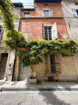 Arles, France - 24.04.2023. Street view of Arles, in the south of France. Facade of old residential building covered ivy or vine plant and with shutters on windows. Charming terracotta houses with gre