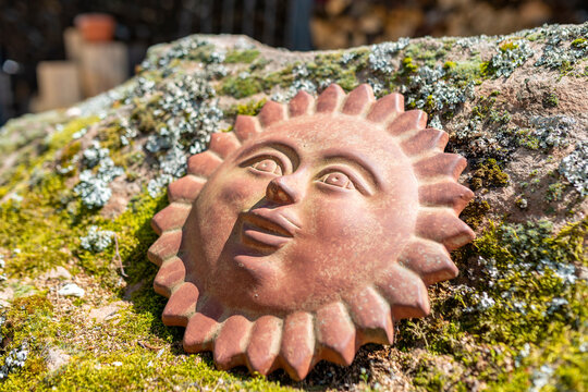 A happy looking sun figure made of red clay lays on a rock.