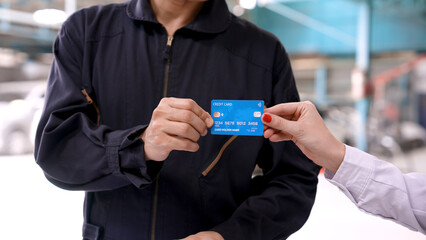 Close-up shot of hand of man and woman handing credit cards to each other, man accepting credit card. It is a non-cash payment to the garage that completes the repair of the car.