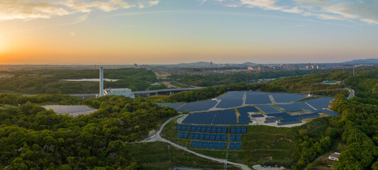 Sunset color in sky over solar farm with distant small town in green landscape