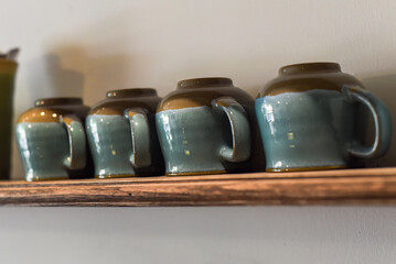 Many blue cups in a row on the woden shelf in the kitchen