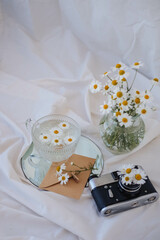Fototapeta na wymiar A bouquet of daisies in a glass vase and an old camera on a white bed.