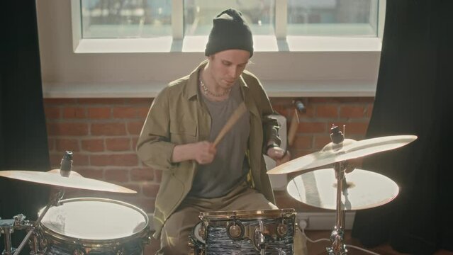 Medium shot of young adult man playing drums indoors in studio