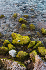 Rocks on the shore of the blue mediterranean sea some covered with green moss