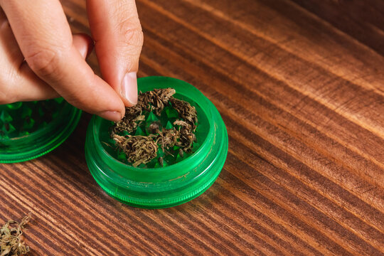 Detail view of cannabis flowers in a grinder on a wooden table.