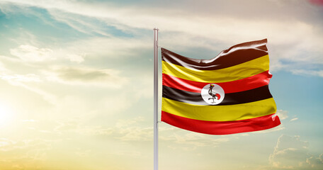 Uganda national flag waving in beautiful sky. The symbol of the state on wavy silk fabric.