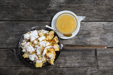 Kaiserschmarrn in eiserner Pfanne mit Apfelbrei auf einem Holztisch angerichtet. Von oben fotografiert.