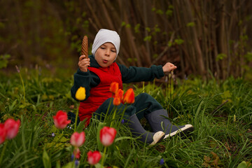 A child with a huge Spruce cone in his hands sits in the woods on a rainy day. Selective focus.