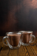 Two mugs of hot chocolate sit on a wooden table.