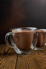 Two mugs of hot chocolate sit on a wooden table.