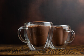 Two mugs of hot chocolate sit on a wooden table.