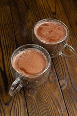 Two mugs of hot chocolate sit on a wooden table.