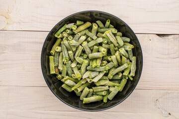 Frozen green beans in a black ceramic plate  on a wooden table, macro, top view.