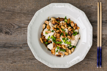 Top view of meal made of silken tofu, roasted peanuts and spring onion, served in white plate. Homemade dish.