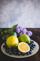 plato con limones y arándanos sobre una mesa de madera, con una flor de lilo detrás
