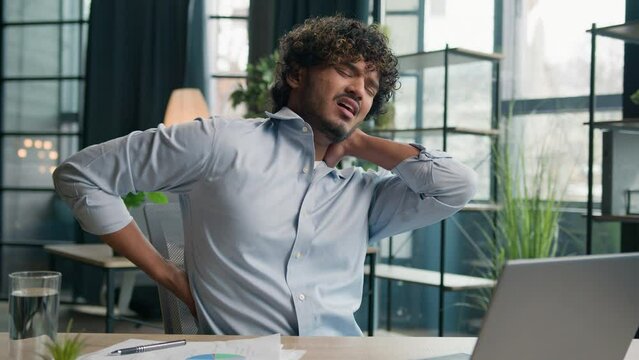 Sick exhausted Arabian Indian latino man feel pain in lower back backache after laptop work unwell ill male guy office manager massaging painful neck relieve ache health problem office syndrome injury