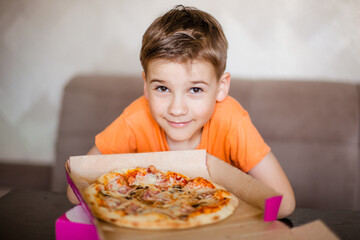 A box of fresh delicious pizza in front of a 7-9 year old boy. The boy is about to eat the pizza it looks delicious right in the box