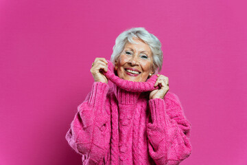 Beautiful and elegant old influencer woman. Cool grandmother posing in studio wearing fashionable clothes. Happy senior lady celebrating and making party. Concept about seniority and lifestyle