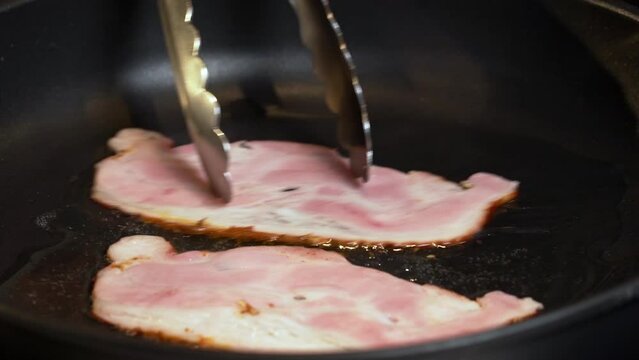 Fry the bacon in a pan. A slice of pork bacon is prepared in its own fat.