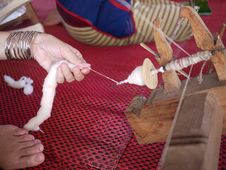 Close up hands of a woman feeds cotton wool into wooden bobbin, traditional spinning wheel to make...