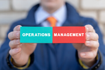 Businessman holding colorful blocks with icons and inscription: OPERATIONS MANAGEMENT. Concept of...