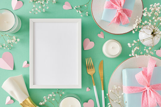 Trendy Mother's Day table setting concept. Top view photo of plate and cutlery napkin gift boxes candles gypsophila flowers and hearts on turquoise background. Flat lay with frame for text or advert