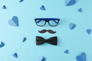 Father's Day celebration concept. Top view flat lay of trendy bow tie glasses black mustache and paper hearts on light blue background - obrazy, fototapety, plakaty