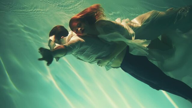 Happy fantasy couple fall in love swim dive man king and woman fashion model posing underwater dark blue sea. Wet white dress. fairy sexy girl Muse river nymph swims hugs guy magic under water pool 4k