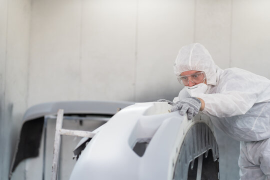 Automotive paint service concept. Male car mechanic inspecting quality of auto body after painting in automotive paint service shop. Automobile painter checking car frame in chamber