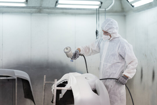Automotive paint service. Quality auto body shop concept. Male car mechanic working with spray gun painting auto body in automotive paint service shop. Automobile painter painting car frame in chamber