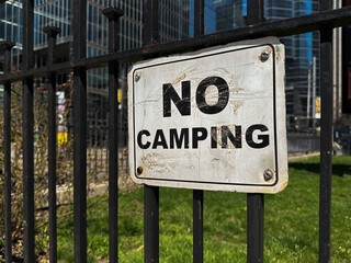 A "no camping" sign on a black wrought iron fence,