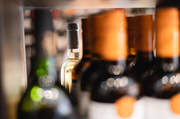 Soft focus of glass bottle filled with white wine placed on shelf with many alcoholic drinks in...