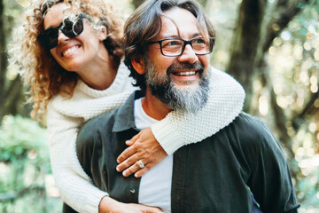 Fototapeta premium Couple of tourist enjoy alternative travel destination in green forest with trees and nature around. Man carrying woman in piggyback. Bonding boyfriend. Husband and wife vacation in nature together