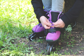 Sunny spring day, a blonde girl sits on the park and puts on roller skates