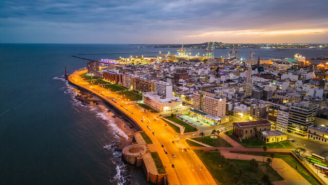 Fototapeta aerial above Montevideo capital city of Uruguay cityscape at night with port and modern buildings over the coastline during sunset