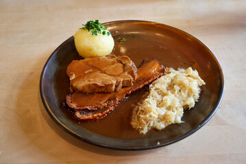 Auf einem Teller liegen ein Kartoffelkloß, Schweinebratenscheiben und Sauerkraut.
